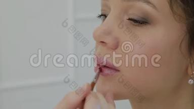 化妆师用刷子在嘴唇上涂口红美丽的女人。 唇部涂抹唇彩